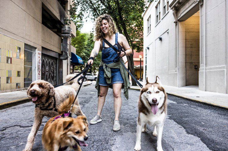 A young woman smiling while walking three dogs down an urban street