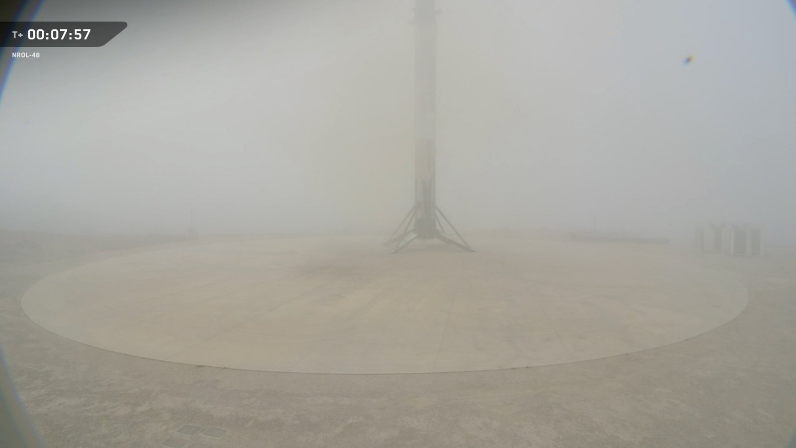 a rocket sits on a tan landing pad, mostly obscured by fog