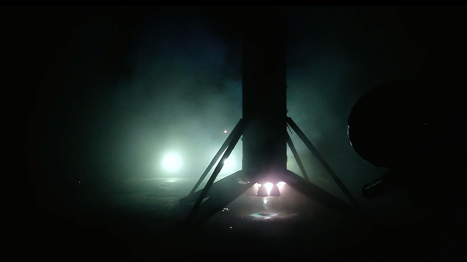 SpaceX Falcon 9 launches 29 Starlink satellites into low Earth orbit from Florida the first stage of an orbital rocket is seen in silhouette, backlit by spotlights, as it stands upright on its landing legs atop an ocean-based droneship.