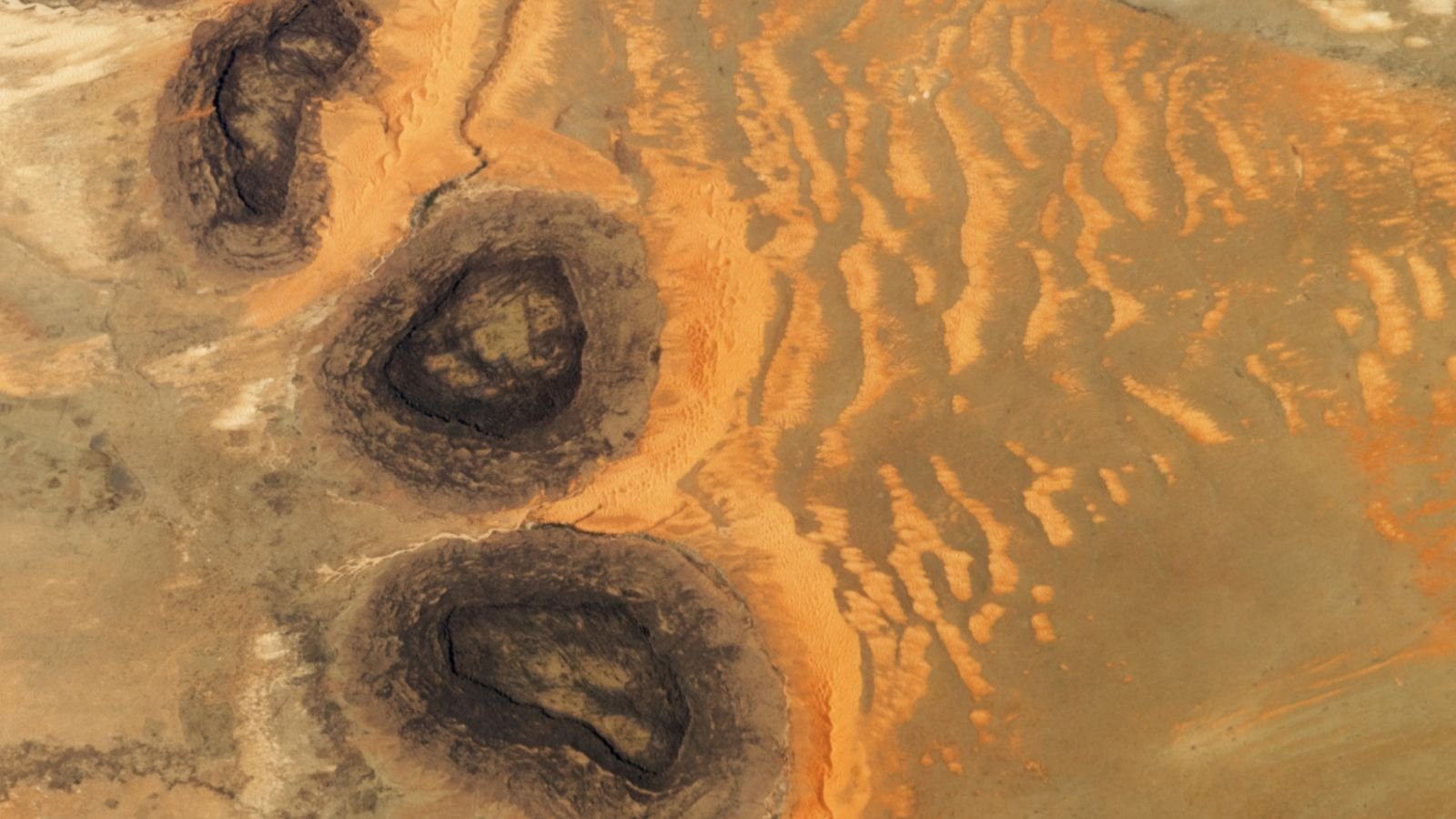 Trio of black mesas leftover from Paleozoic era spawn rare sand dunes in the Sahara